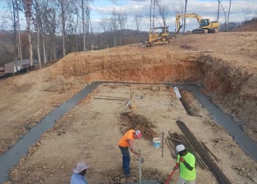 Foundation footer and slab pour in progress with excavator on a hillside job site in Tennessee